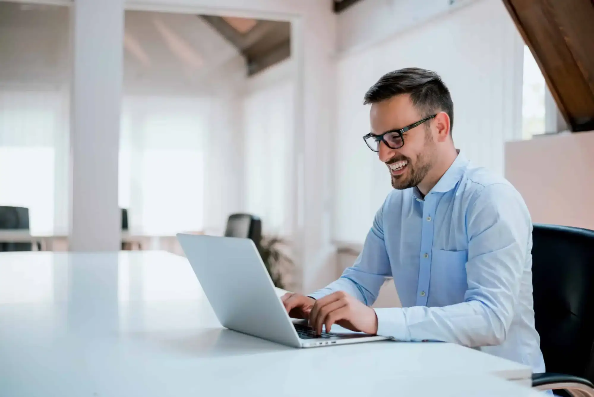 Smiling professional in glasses working on a laptop in a bright modern office