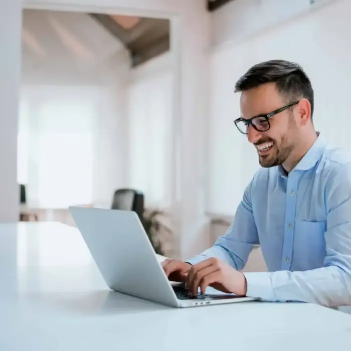 Smiling professional in glasses working on a laptop in a bright modern office